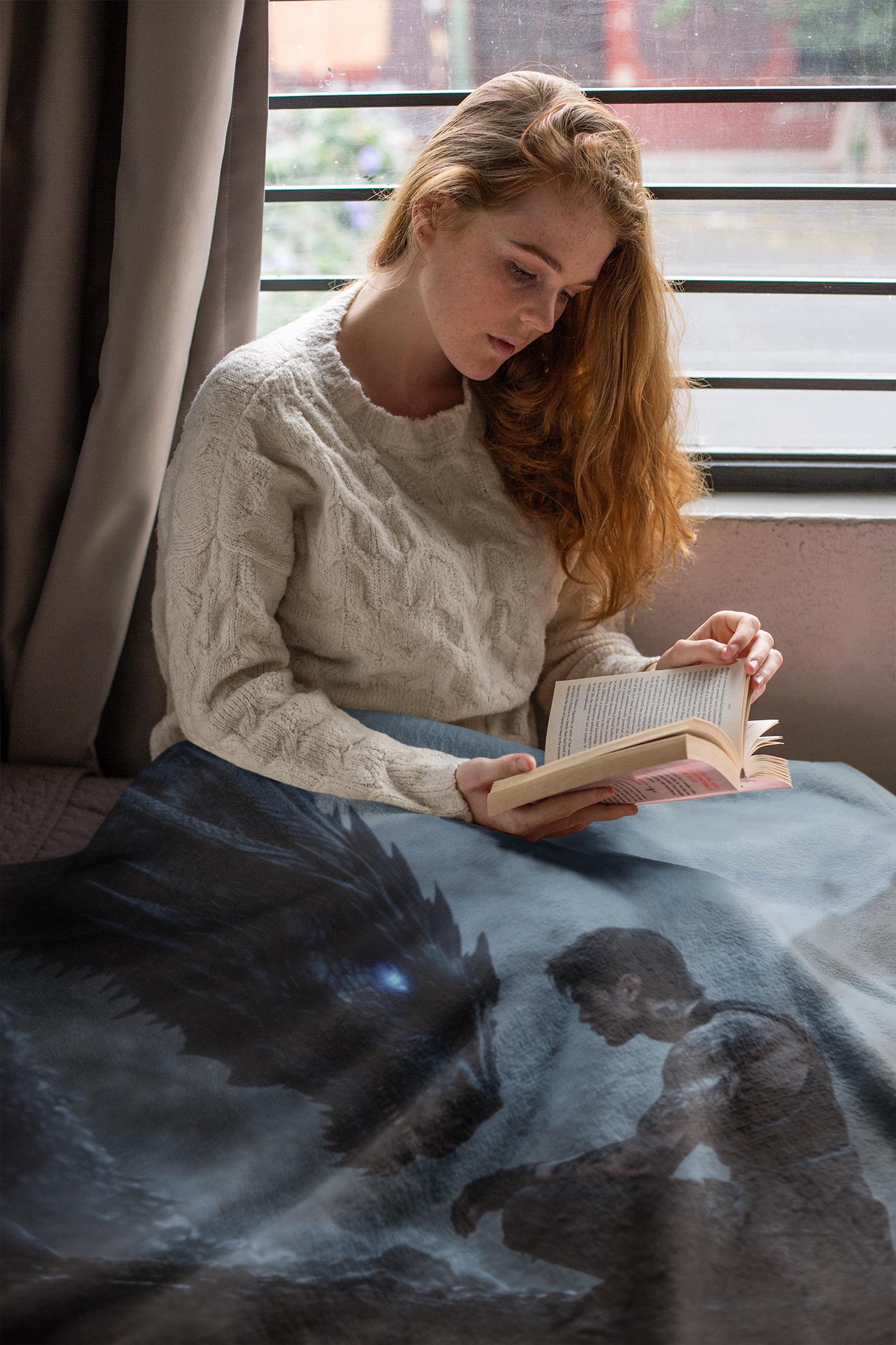 Woman reading a book on a bed with a blanket featuring a space-themed design.